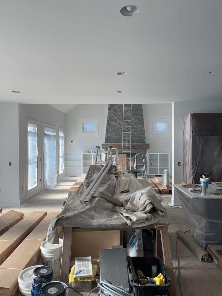 A bright, spacious room under construction with a large stone fireplace, drop cloths, building materials, and tools.