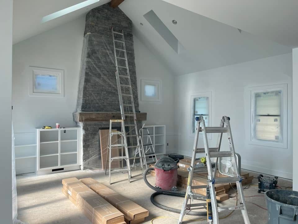 A room under renovation featuring a tall stone fireplace, two step ladders, building materials, and a shop vacuum.