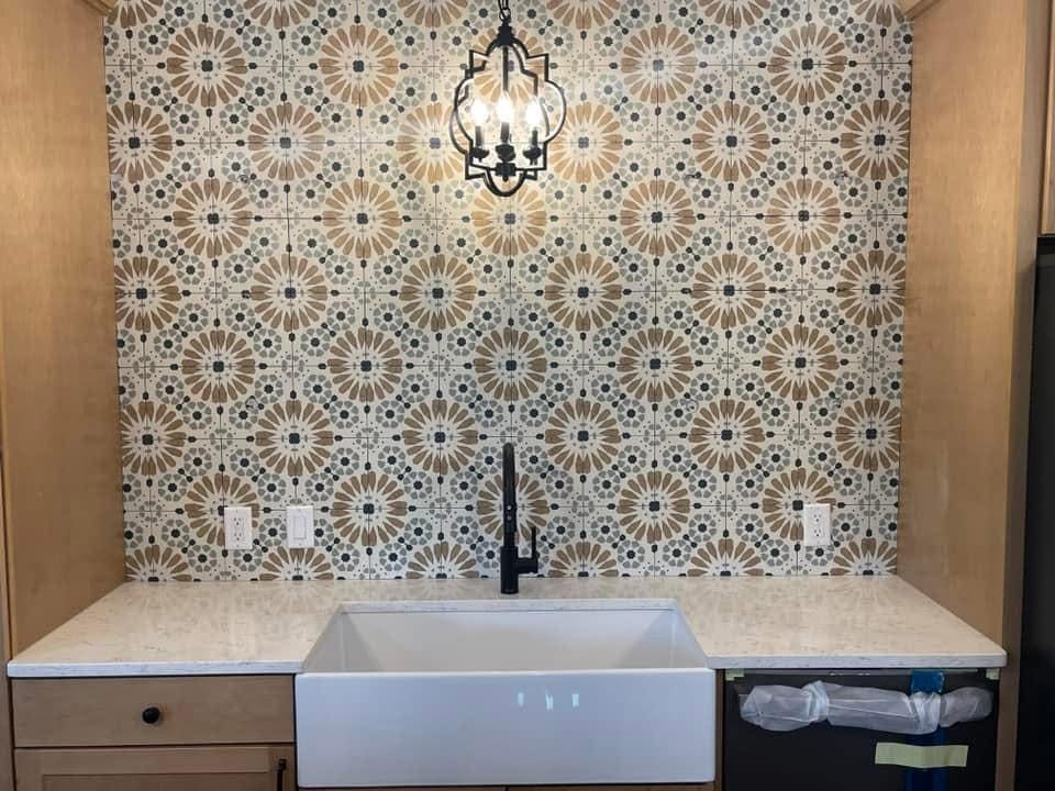 A white farmhouse sink and faucet set against a decorative tile backsplash with a geometric tan and blue pattern.