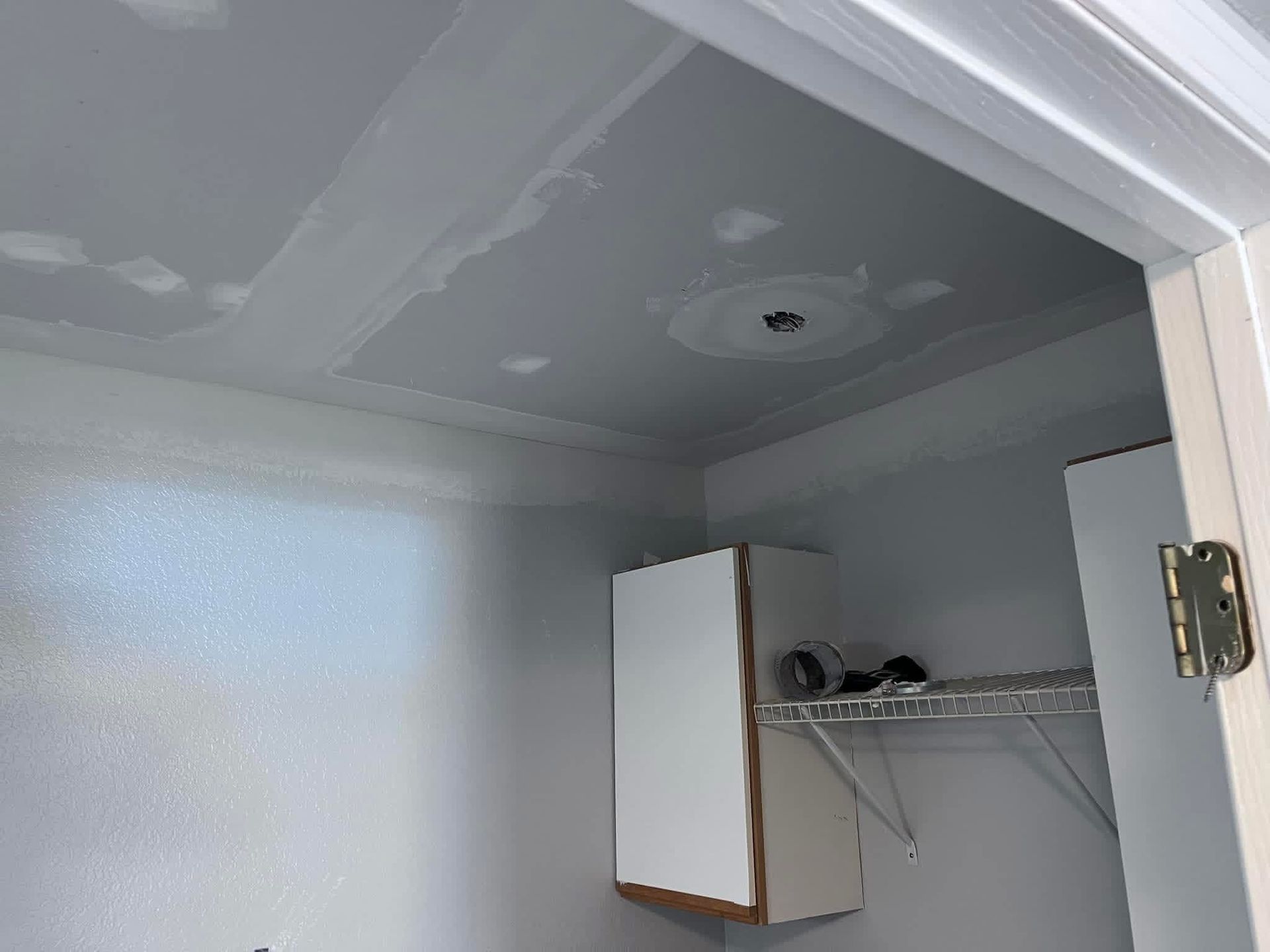 A small closet interior with a gray, unfinished drywall ceiling showing joint compound patches, a cabinet, and wire shelving.
