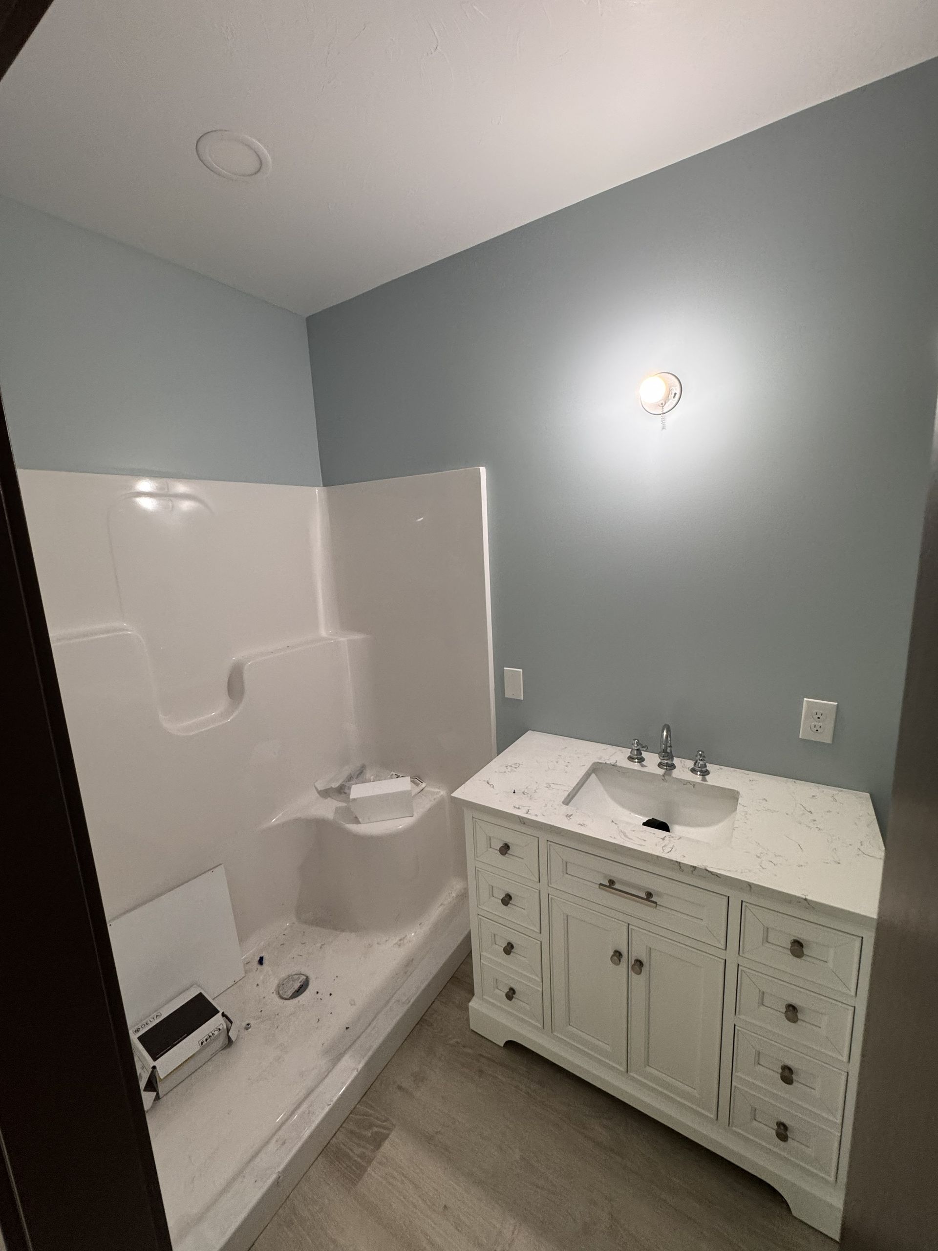 A bathroom with light blue walls, a white vanity with a marble top, and a white shower stall with a built-in seat.