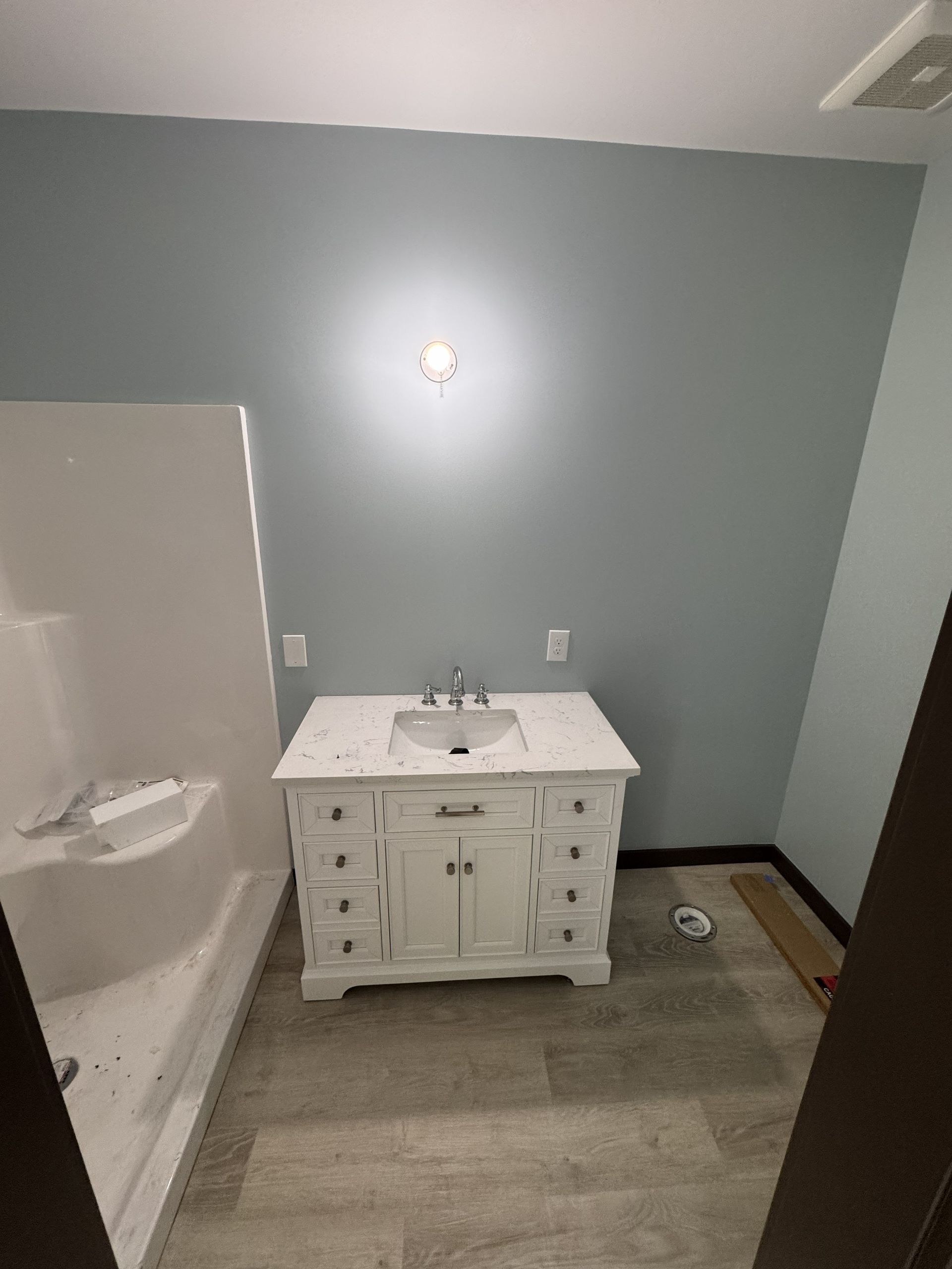 A bathroom vanity with a white cabinet and marble countertop against a blue wall, next to a white shower stall.