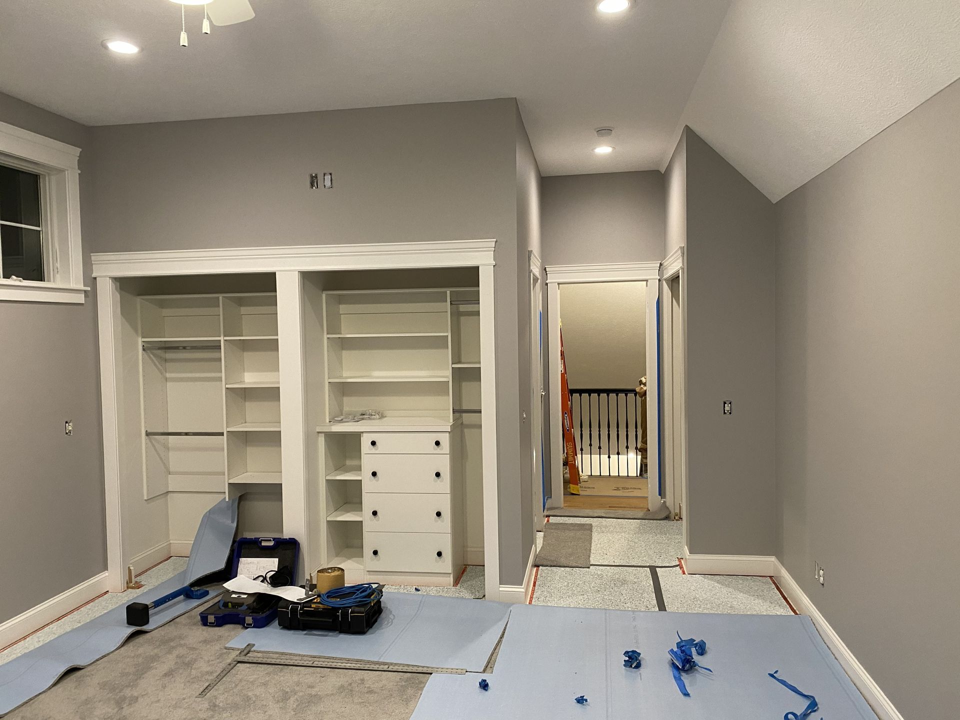 A room under renovation with gray walls, white built-in shelving, and protective floor covering.
