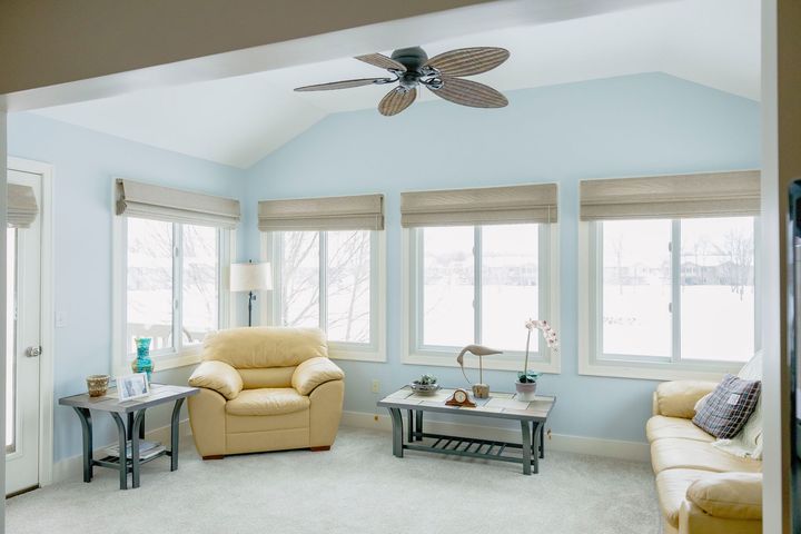 A sunroom with light blue walls, featuring a cream armchair, a glass coffee table, and a matching sofa near bright windows.