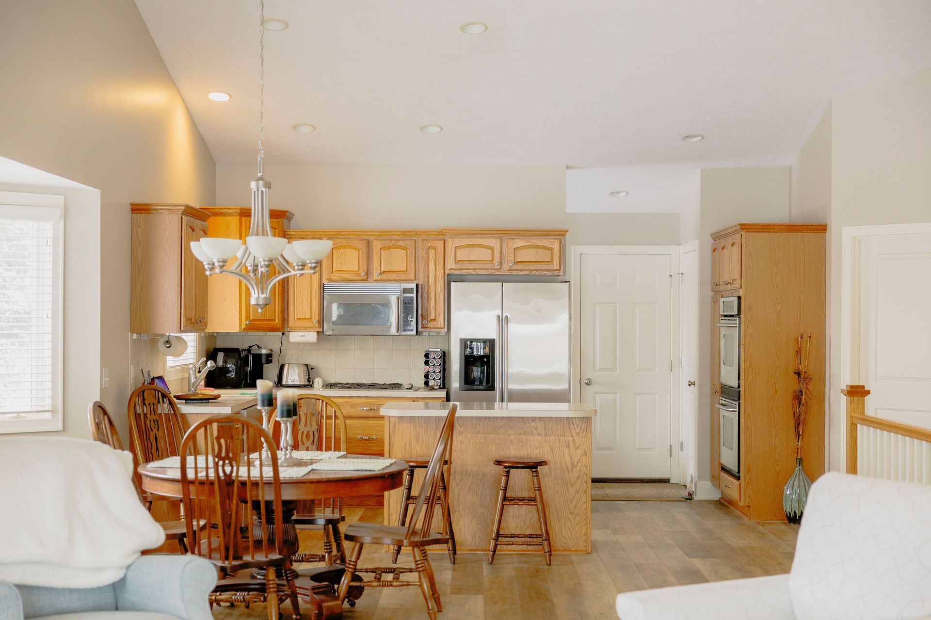 A bright kitchen with light wood cabinets, stainless steel appliances, a dining table, and a wooden island with a stool.