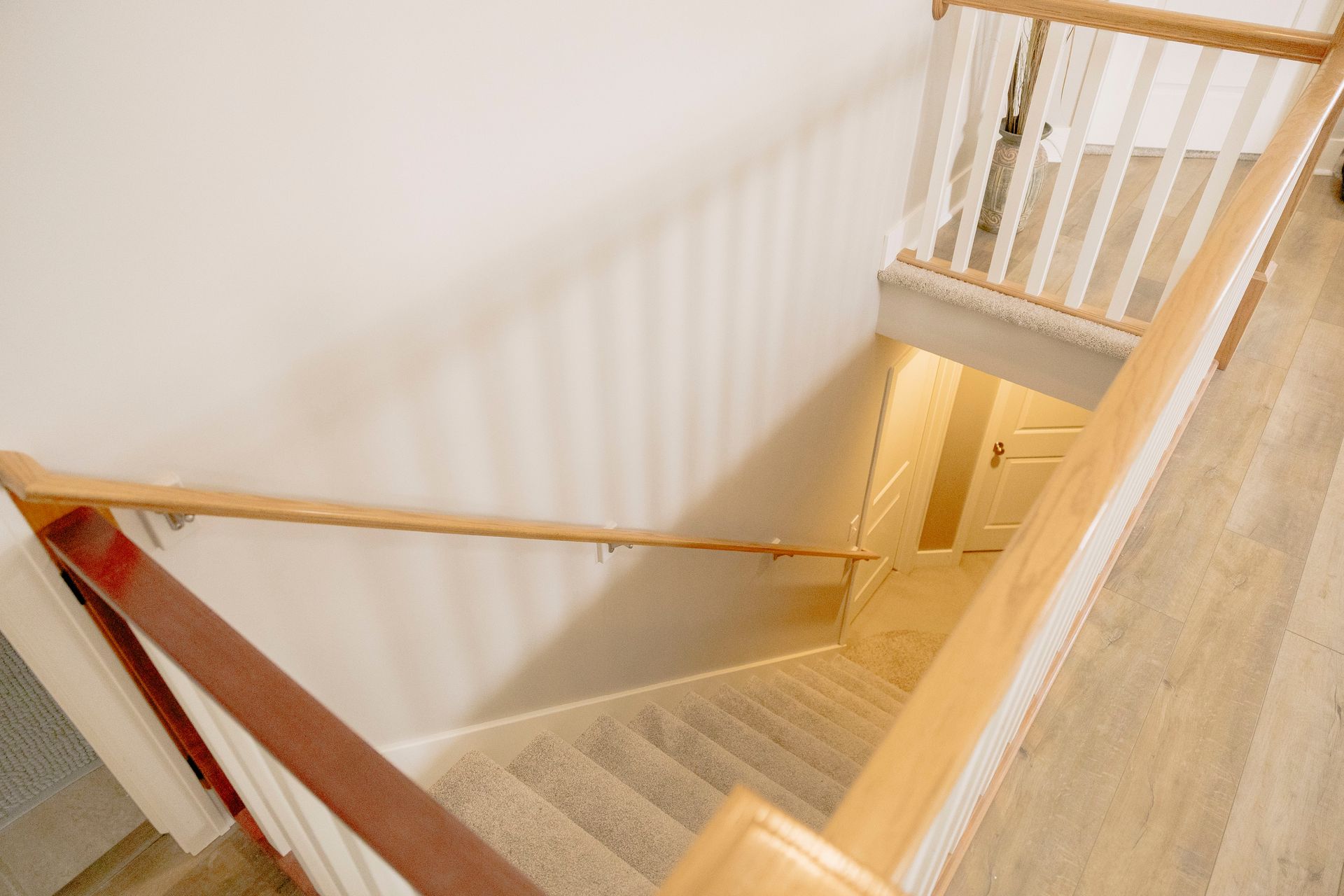 An elevated view of carpeted stairs leading downward, framed by a light wood handrail and a white railing.