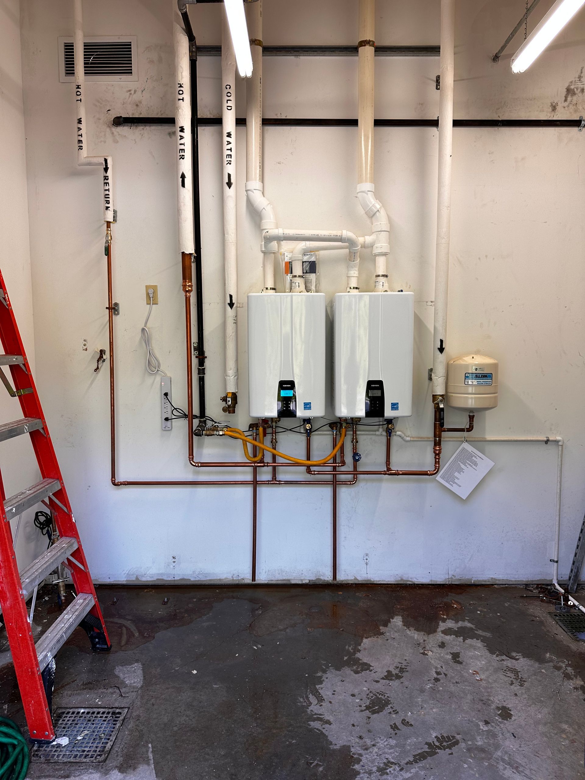 A room with a ladder and two water heaters on the wall