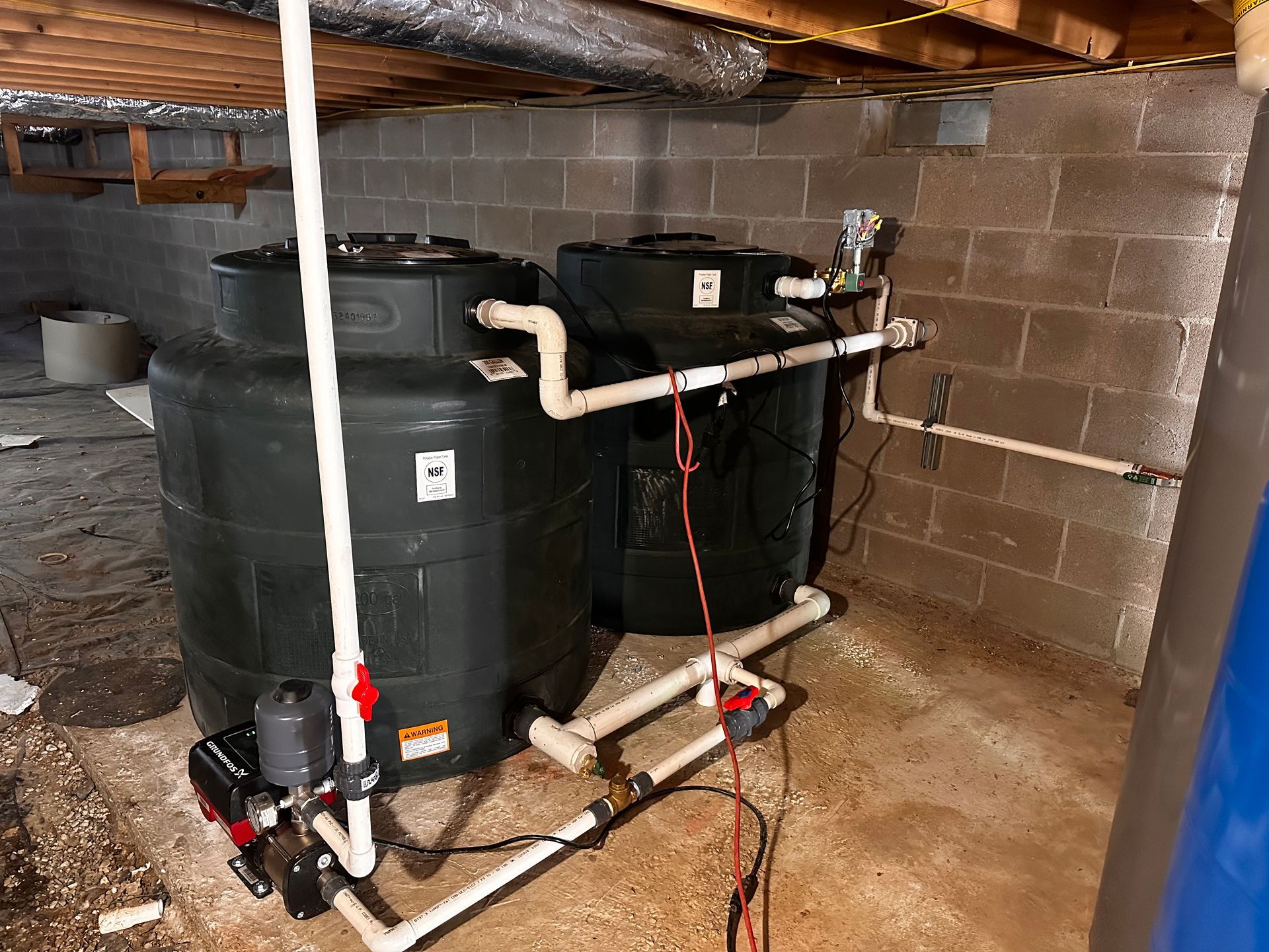 Two black tanks are sitting in a basement under a brick wall