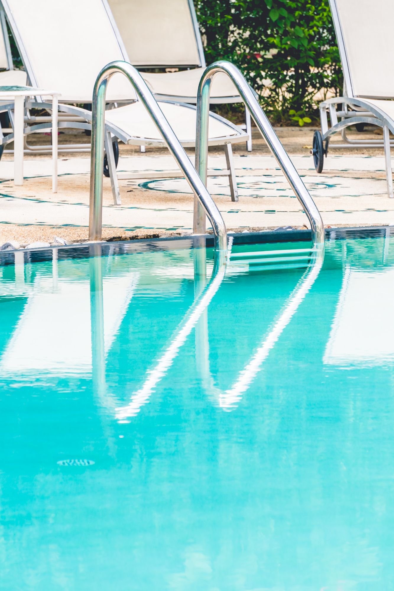 A swimming pool with chairs and stairs leading to it.