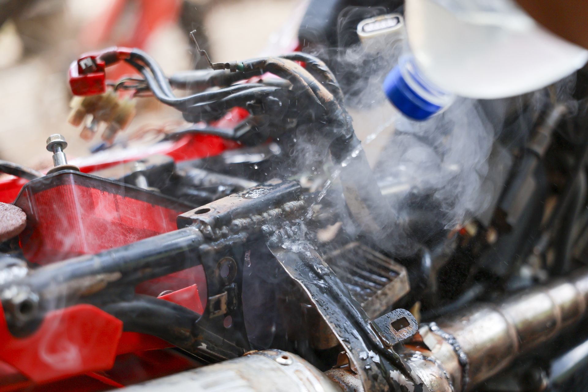 Mechanic cleaning a bike engine with a spray hose, water and steam visible.