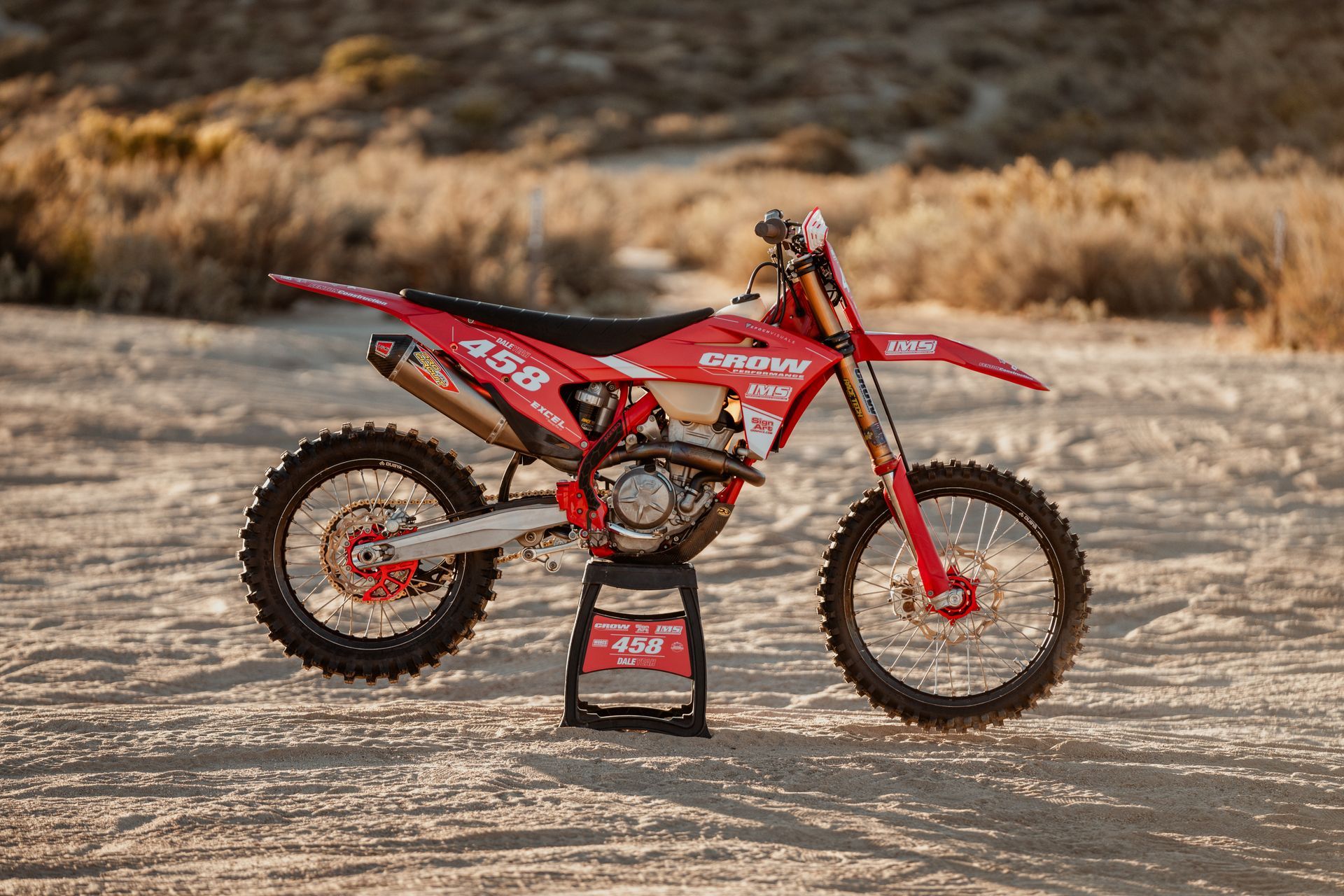 Red motocross dirt bike on a stand in a rocky desert setting