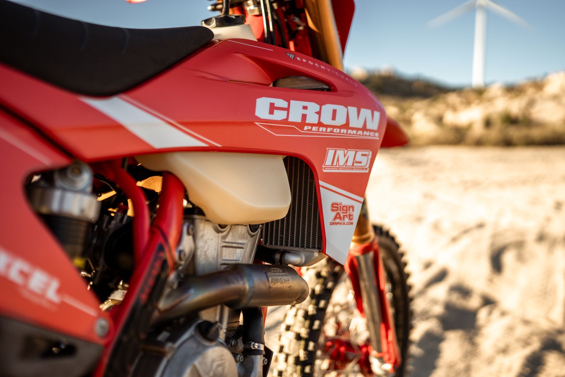 Red off-road motorcycle with CROW branding on a sandy trail in bright sunlight