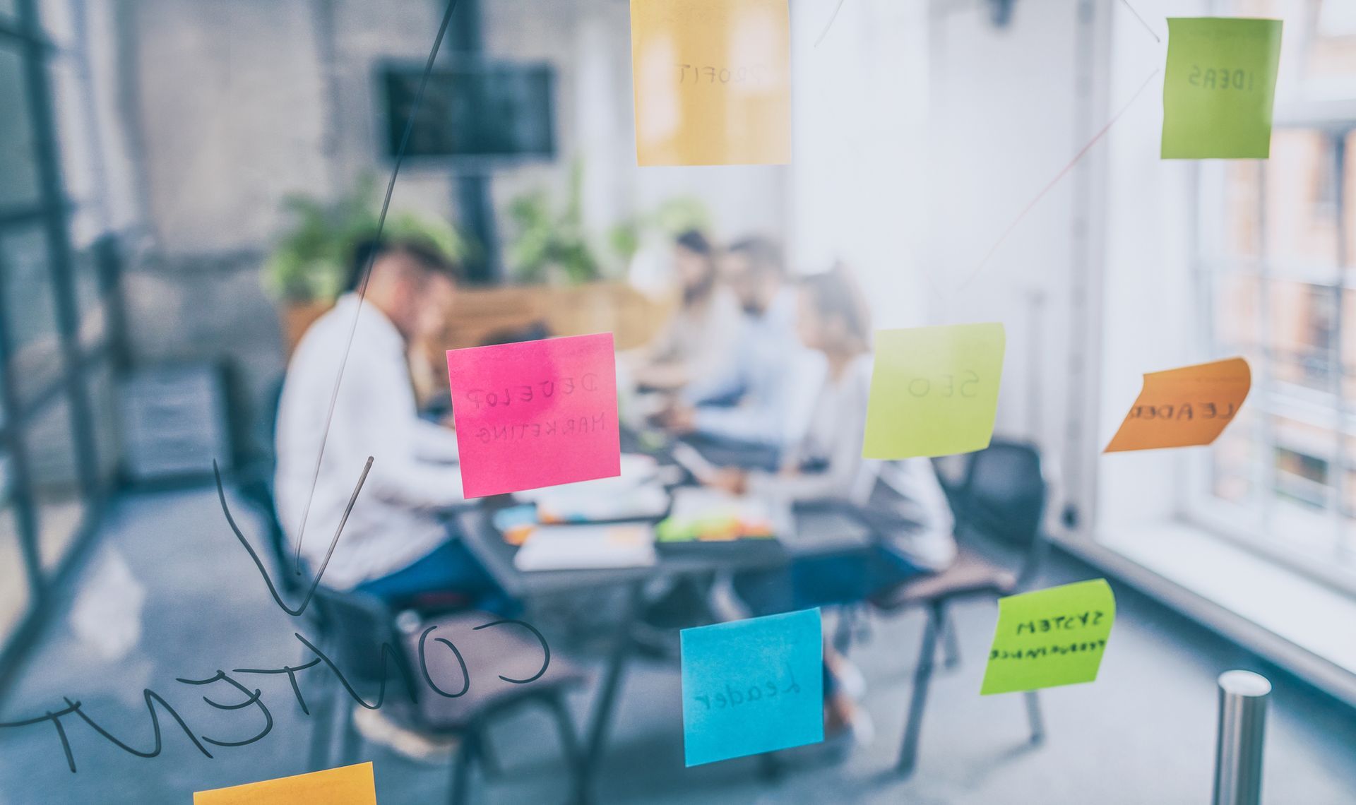 A group of people are having a meeting in a conference room with sticky notes on a glass wall.
