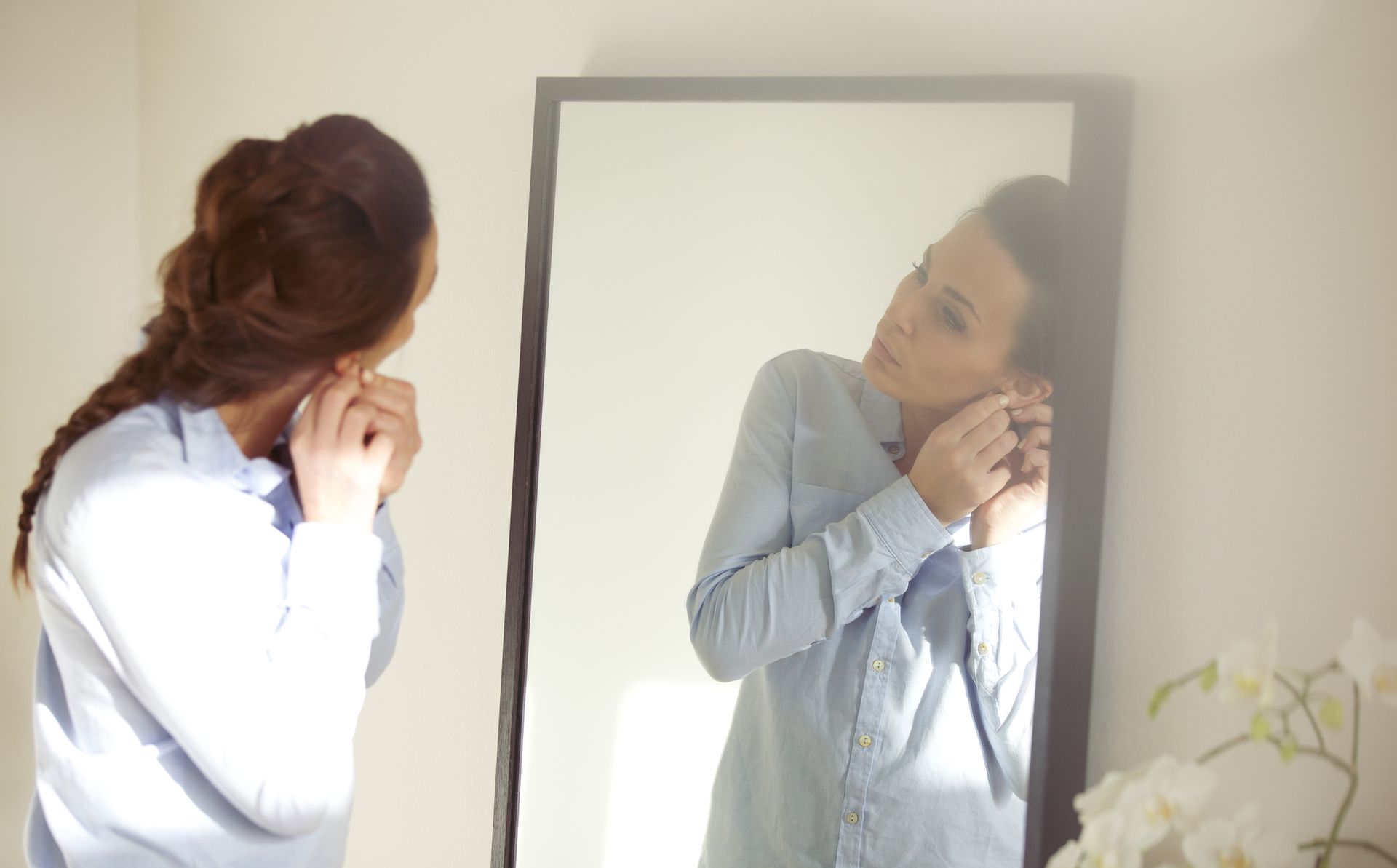 A woman is putting on her earrings in front of a mirror.