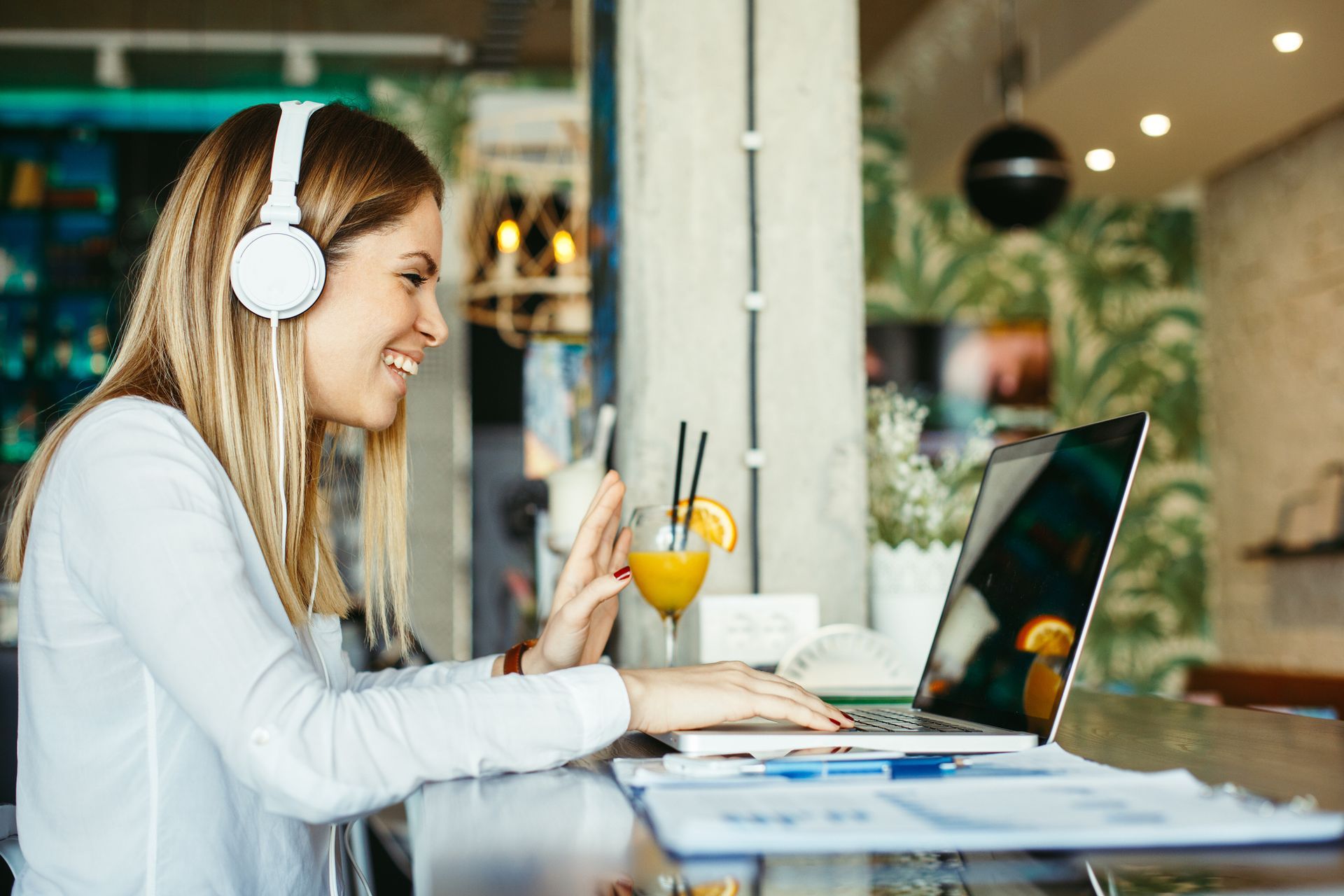 A woman wearing headphones is sitting at a table using a laptop computer.