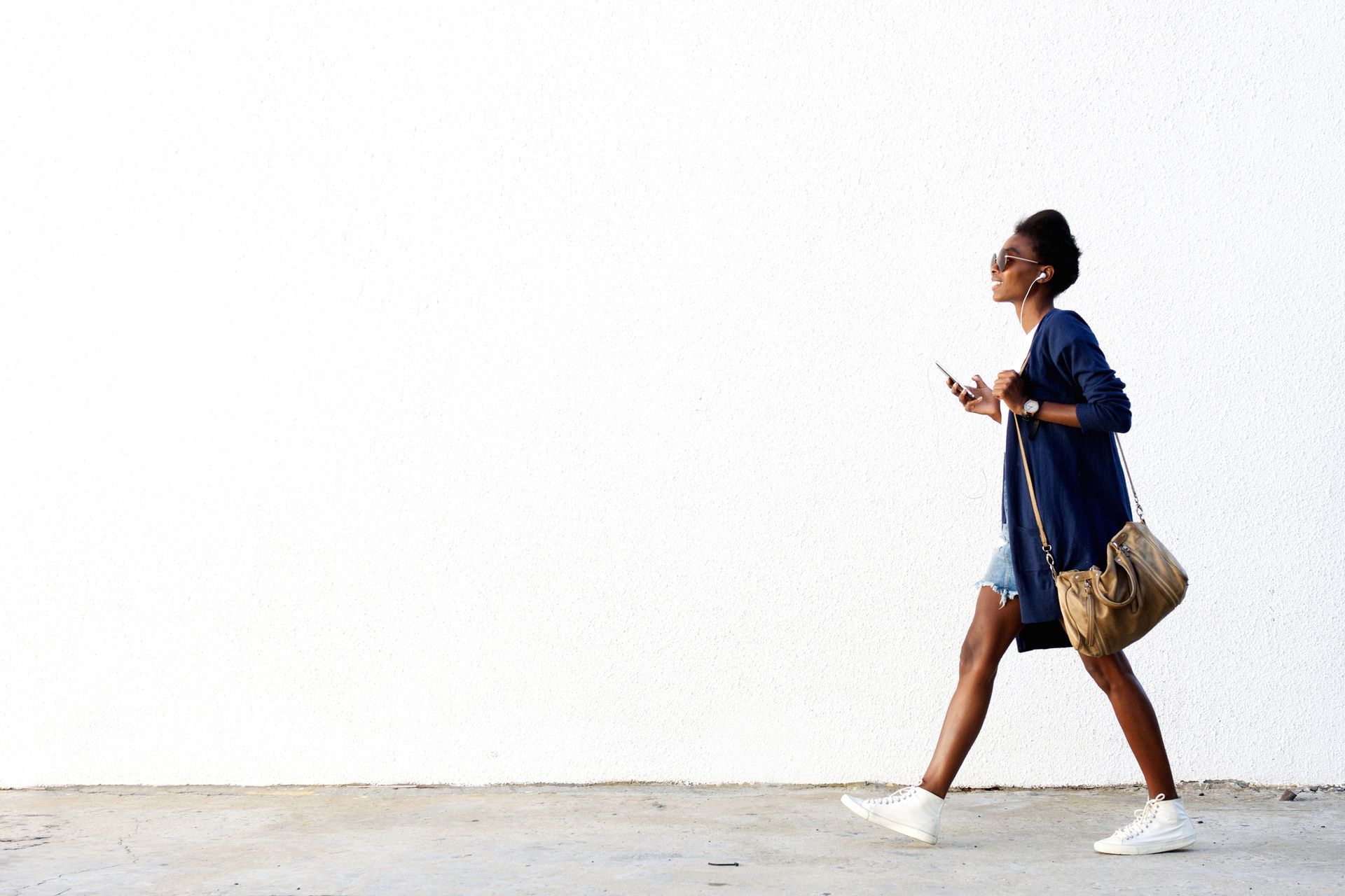 A woman is walking down the street while looking at her phone.
