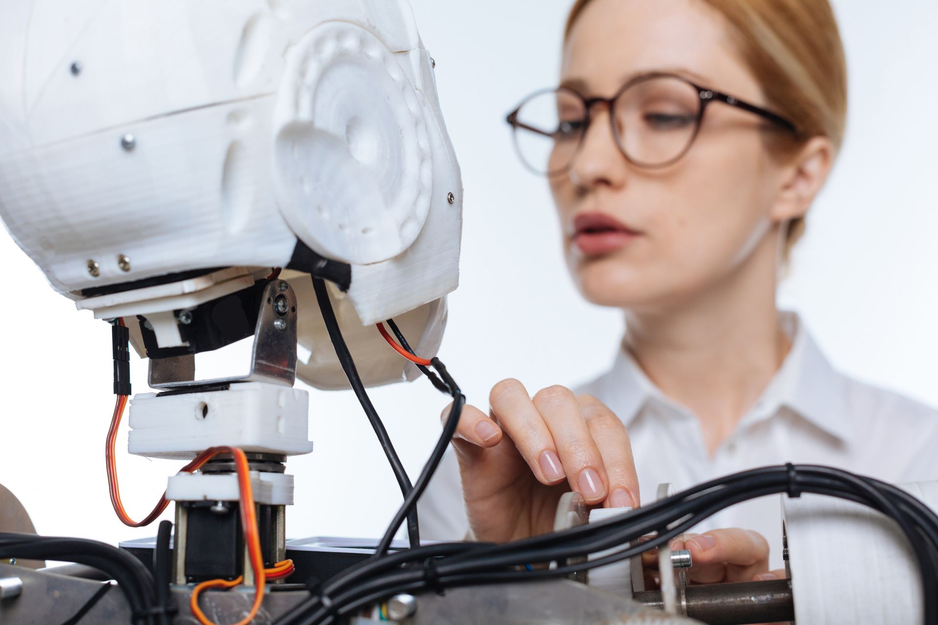 A woman wearing glasses is working on a robot.