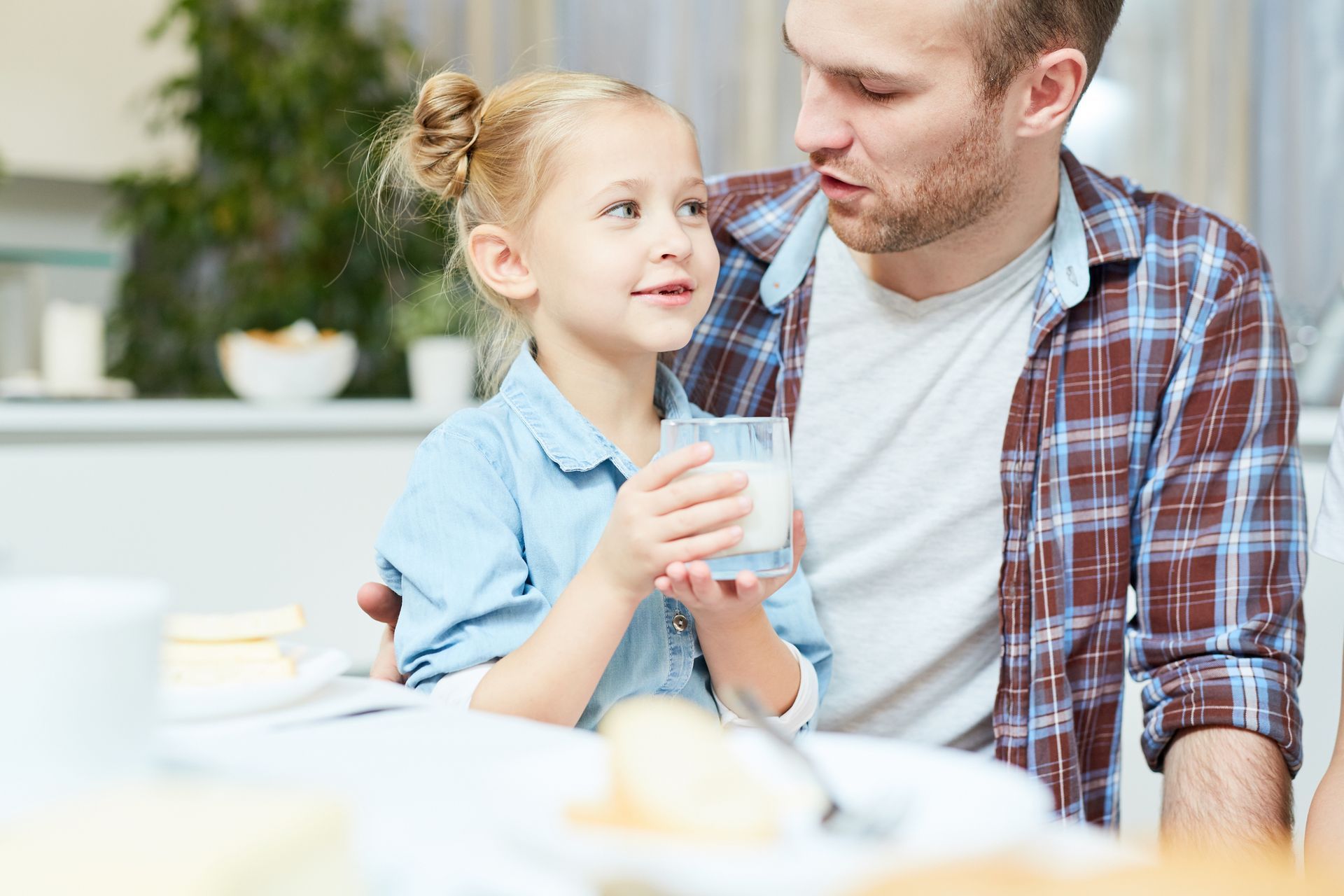 A man is holding a little girl who is drinking a glass of milk.