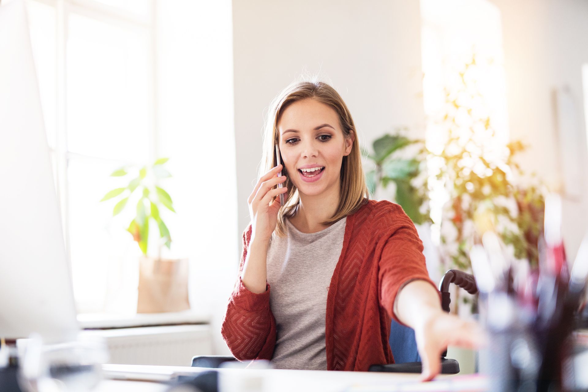A woman is sitting at a desk talking on a cell phone.