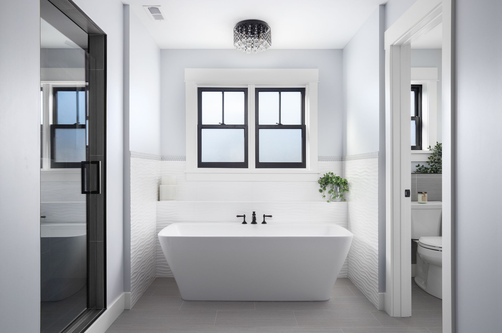 Modern bathroom with glass shower, freestanding tub, and chandelier lighting.