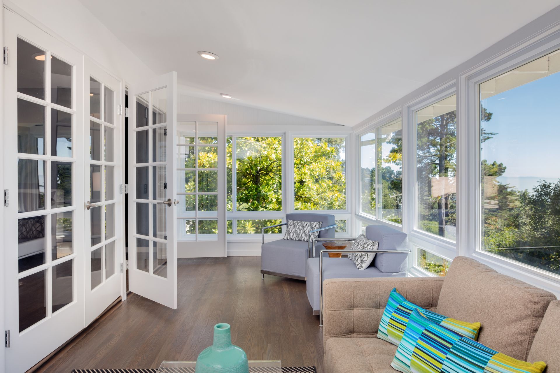 Bright sunroom with floor-to-ceiling windows, French doors, seating area, and wood flooring.