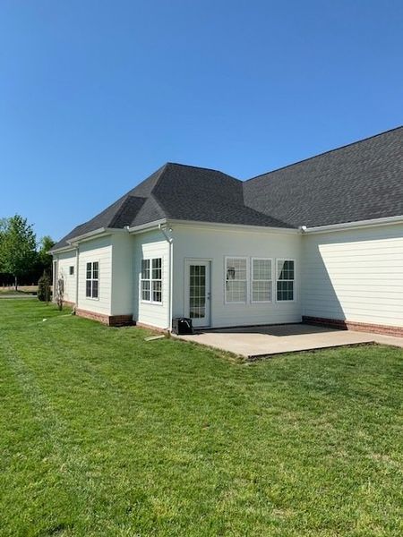 White house with dark roof, small patio, and green lawn under a clear blue sky White house with dark roof, small patio, and green lawn under a clear blue sky.