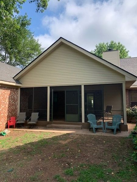 Back patio with sliding glass doors, brick walls, and two turquoise chairs beneath a beige gable roof.