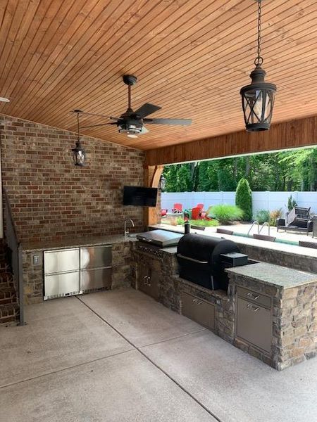 Covered outdoor patio with brick bar, ceiling fans, lanterns, and seating by a pool