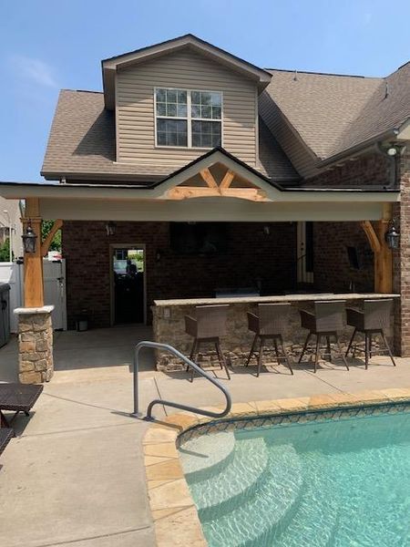 Backyard patio with covered bar seating beside a swimming pool and tan brick house