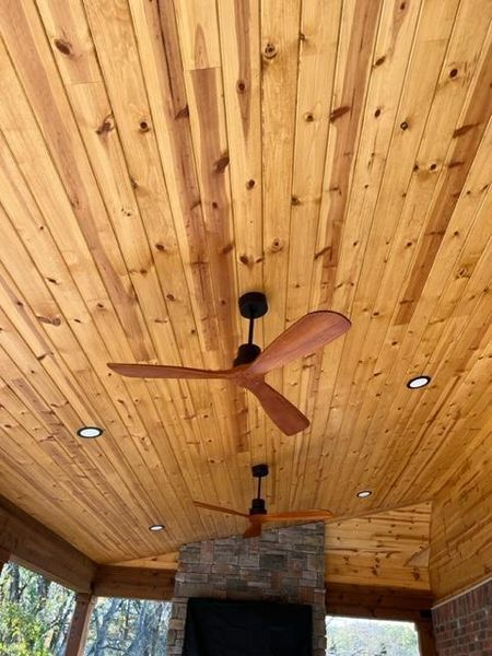 Wood-paneled porch ceiling with a brown ceiling fan and recessed lights above a brick fireplace.