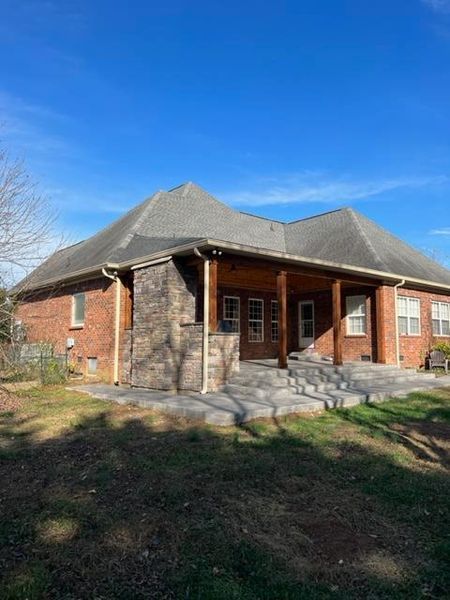 Single-story brick house with a gray roof, front porch, and stone steps in a sunny yard.