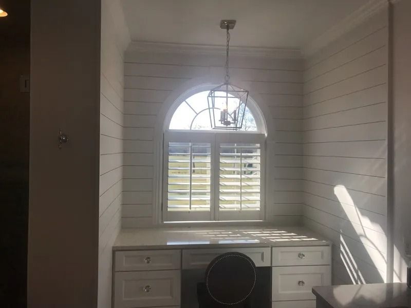 Bright white room with desk, arched window, and sunlight casting shadows on paneled walls