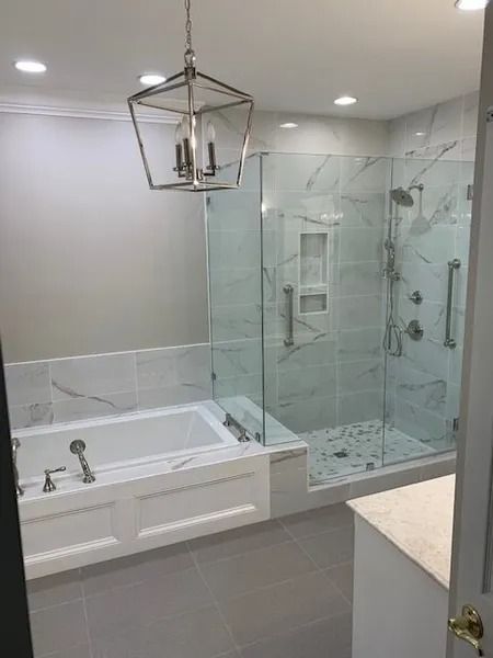Bright modern bathroom with glass shower, bathtub, gray tile, and pendant light