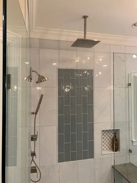Glass shower with wall-mounted showerhead, handheld wand, and tiled accent panel in a bathroom.