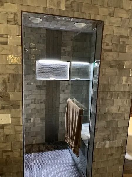Small tiled shower stall with glass door and a towel hanging inside.
