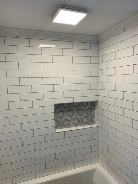 White-tiled shower alcove with a recessed niche and ceiling light.