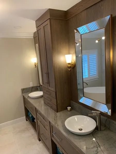 Elegant bathroom vanity with wood cabinets, gray stone countertop, and wall mirror beside a window.