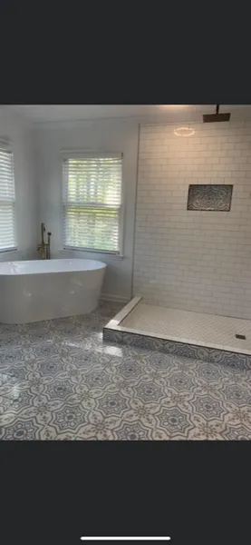 Bathroom with freestanding tub, glass shower, white tile walls, and patterned gray floor.