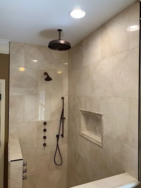 Modern beige tiled shower with a black rainfall showerhead and hand wand, plus a recessed niche.