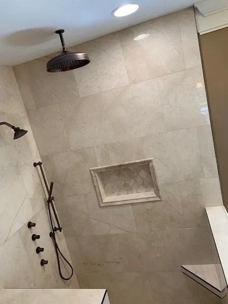 Modern beige tiled shower with black fixtures, handheld sprayer, and recessed shelf.