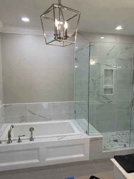 Luxurious bathroom with a soaking tub, glass shower, marble walls, and a geometric pendant light.