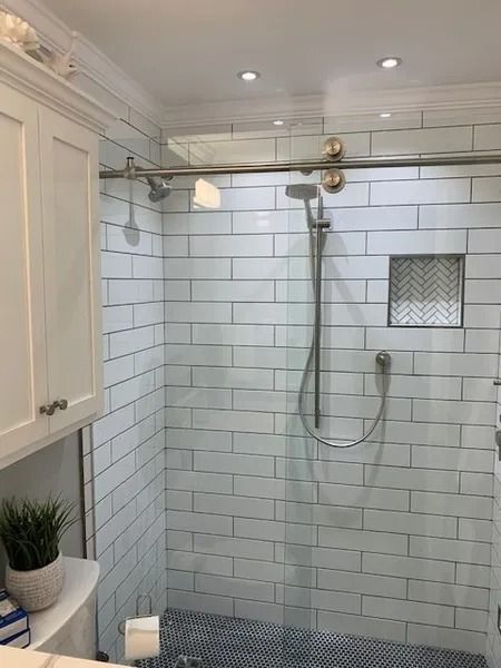 White-tiled shower with brass fixtures, handheld showerhead, and a built-in niche in a bathroom.