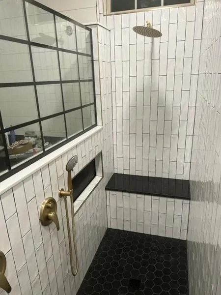 Small tiled shower area with black hex floor, white walls, glass partition, and brass fixtures