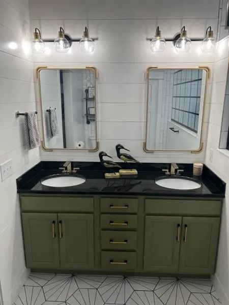Green bathroom vanity with two mirrors, black countertop, sinks, and wall sconces.