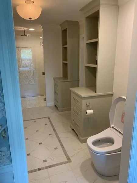 Bright bathroom with built-in shelves, cabinets, tiled floor, and a toilet in the foreground.