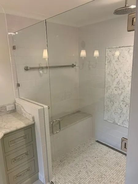 Bright bathroom with glass shower enclosure, marble-tile floor, and white vanity cabinet