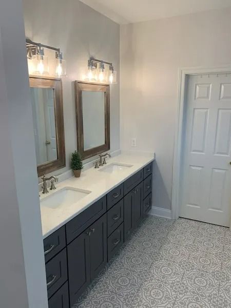 Modern bathroom with double vanity, large mirrors, wall sconces, and patterned tile floor
