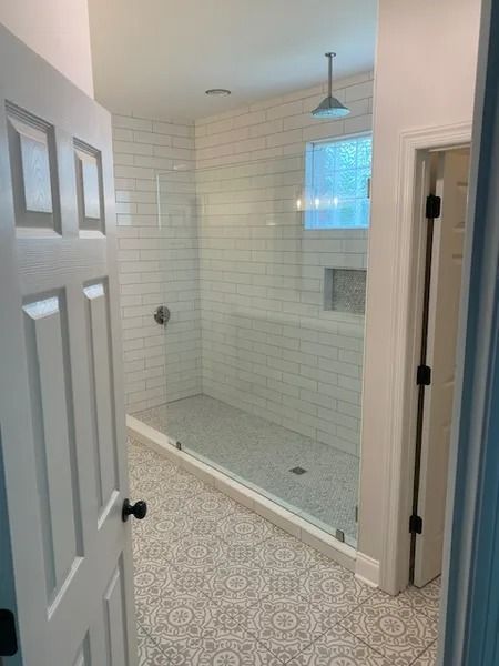 Bright tiled walk-in shower with glass door, bench niche, and window in a bathroom