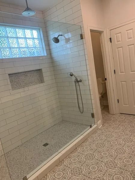 Accessible walk-in shower with white tile, glass block window, built-in niche, and handheld showerhead.