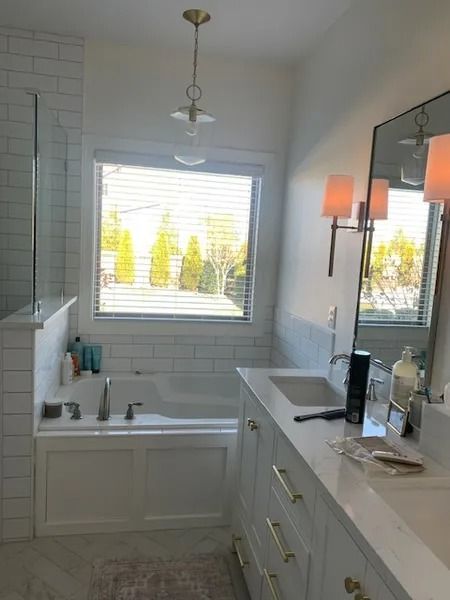 Bright white bathroom with a tub, vanity, window, and wall mirror over the sink.